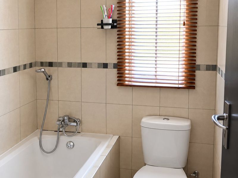 A clean, functional bathroom featuring neutral wall tiles, a built-in bathtub with a handheld shower mixer, and a standard toilet.