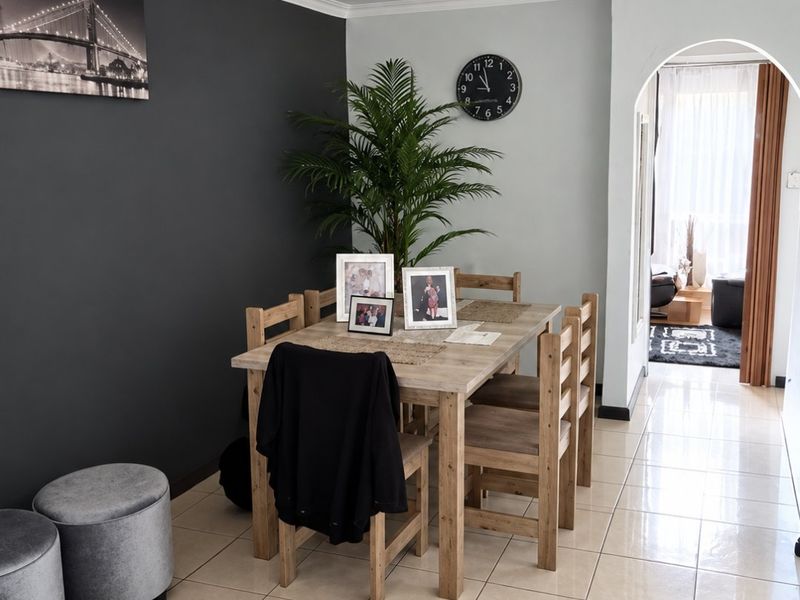 A well-maintained dining area featuring neutral tiled flooring, a distinct feature wall, and an arched entryway leading to an adjacent living space.