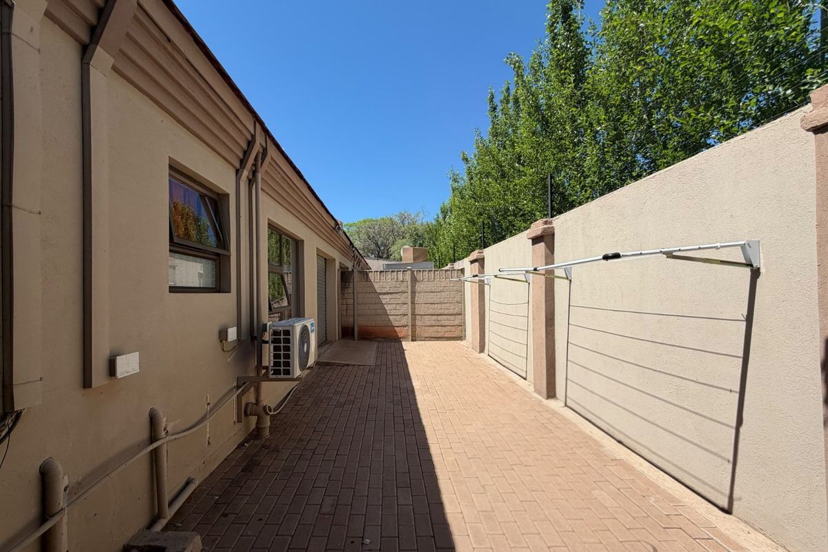 A clean and well-maintained paved side yard featuring a boundary wall, wall-mounted washing line, and an external air conditioning unit.
