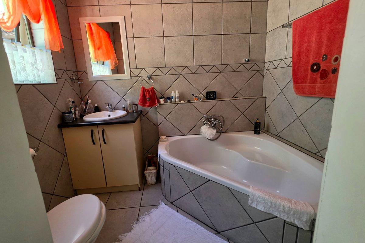 A functional bathroom featuring a corner bathtub, vanity cabinet with basin, and neutral wall tiling throughout.