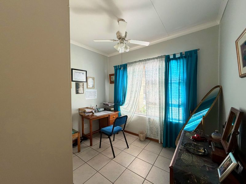 A functional bedroom featuring tiled flooring, a ceiling fan, and natural light through window blinds.