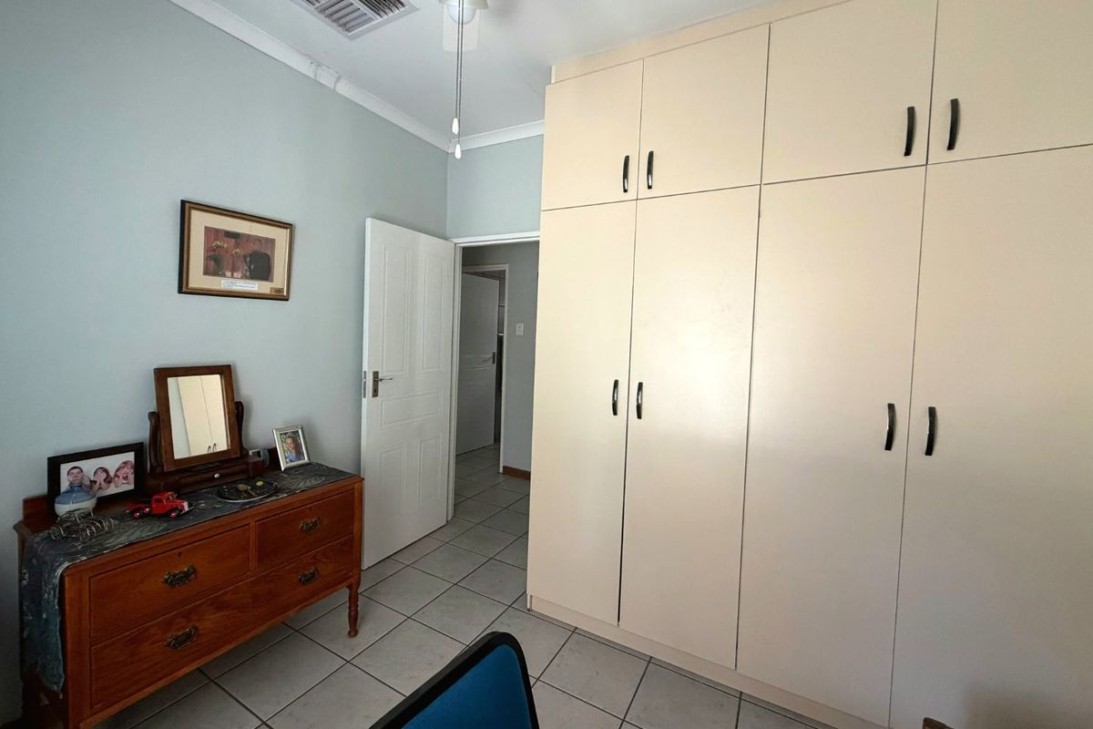 A bedroom featuring built-in cupboards, tiled flooring, and a ceiling fan, offering a functional space with neutral wall tones.