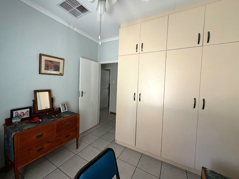 A bedroom featuring built-in cupboards, tiled flooring, and a ceiling fan, offering a functional space with neutral wall tones.