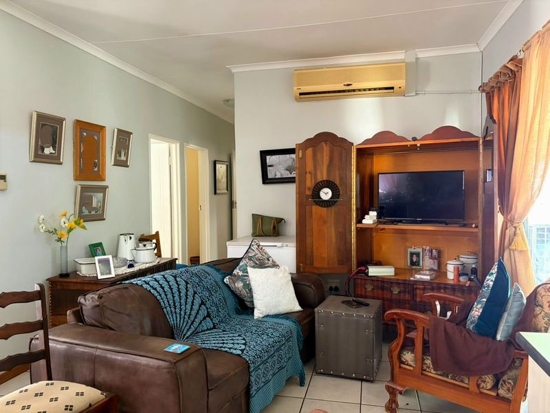 A comfortable living room featuring tiled flooring, coved ceiling cornices, and a wall-mounted air conditioning unit.