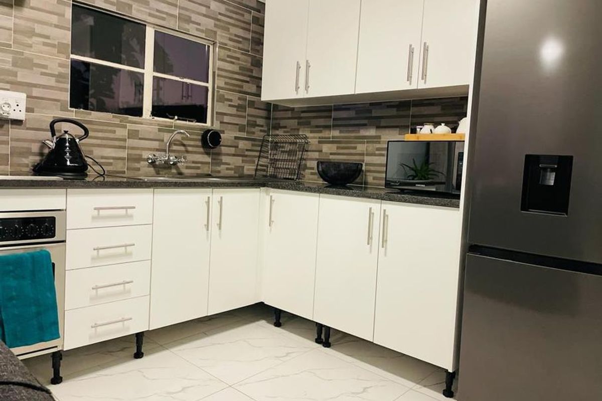 A modern kitchen featuring white cabinetry, dark countertops, a tiled backsplash, and tiled flooring, providing a clean and functional cooking space.