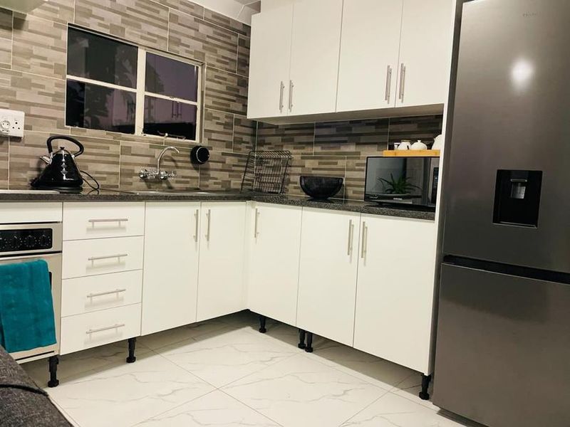 A modern kitchen featuring white cabinetry, dark countertops, a tiled backsplash, and tiled flooring, providing a clean and functional cooking space.