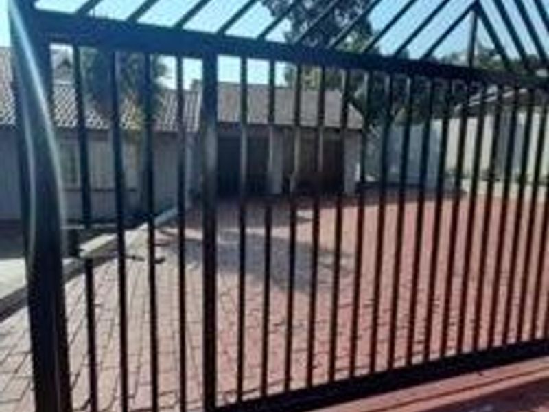 A view of the property entrance featuring a black metal security gate and a paved driveway leading to the main building structure.