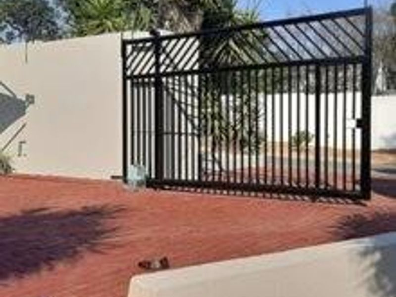 A secure front entrance featuring a black metal sliding gate, paved driveway, and perimeter boundary wall with electric fencing.