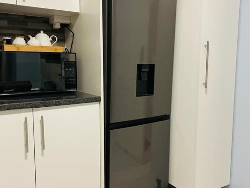 A modern kitchen section featuring white cabinetry, dark countertops, and tiled flooring, with space for a large refrigerator and built-in microwave.