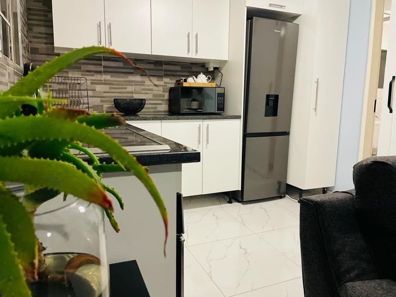 A modern kitchen featuring white cabinetry, stone countertops, a tiled backsplash, and polished floor tiles, offering a clean and functional cooking space.