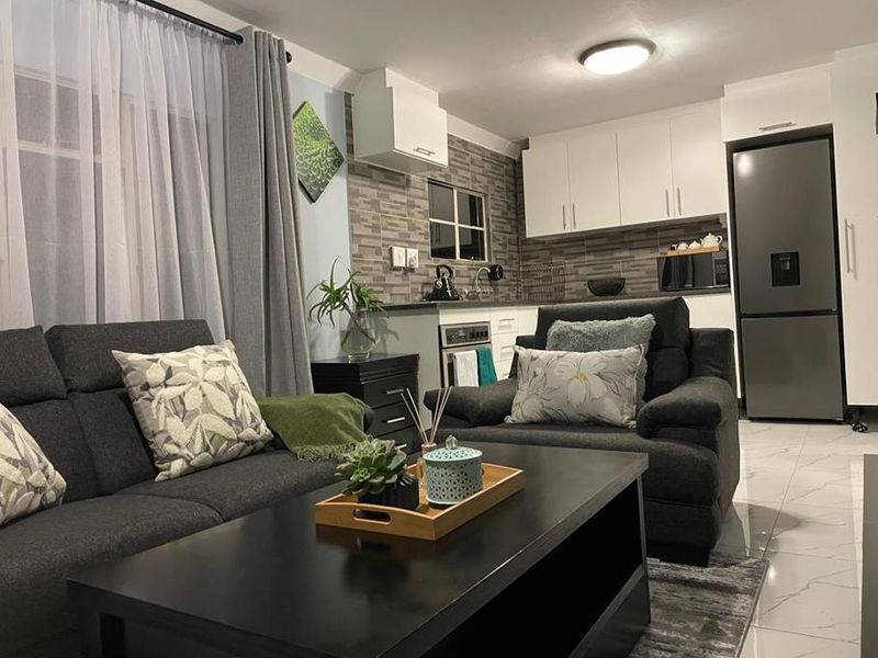 Open plan living area featuring a modern kitchen with built-in cabinetry, tiled backsplash, and integrated oven, seamlessly connected to a comfortable lounge space.