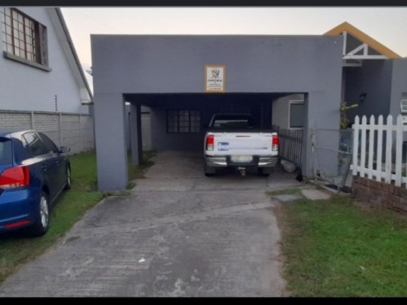 A functional carport structure with a concrete driveway, enclosed by a precast boundary wall and a picket fence.