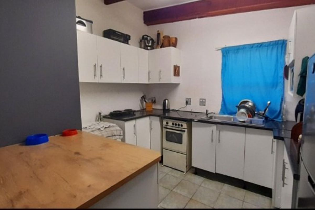 A functional kitchen featuring white cabinetry, laminate countertops, a freestanding oven, and a stainless steel sink with tiled flooring.