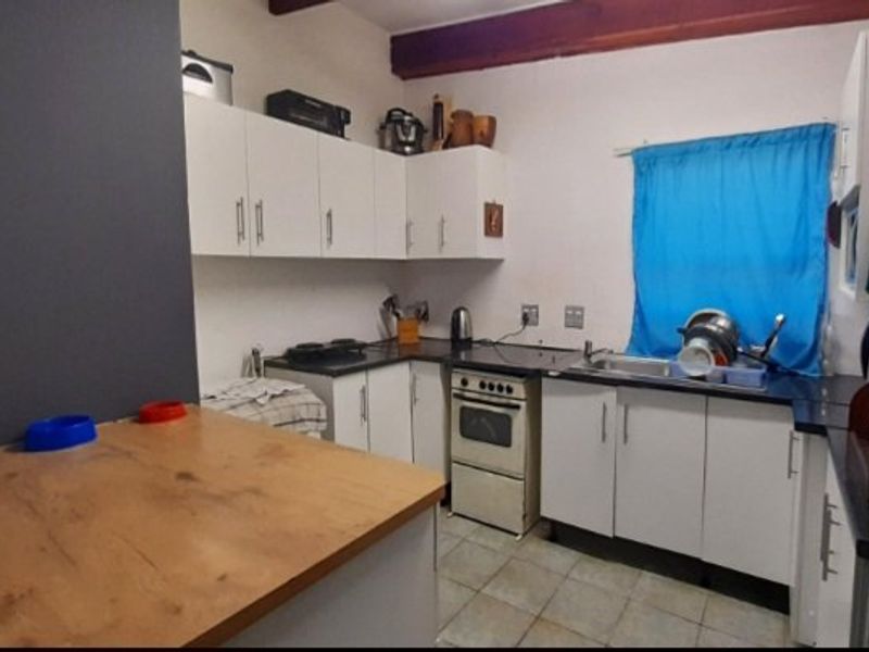 A functional kitchen featuring white cabinetry, laminate countertops, a freestanding oven, and a stainless steel sink with tiled flooring.
