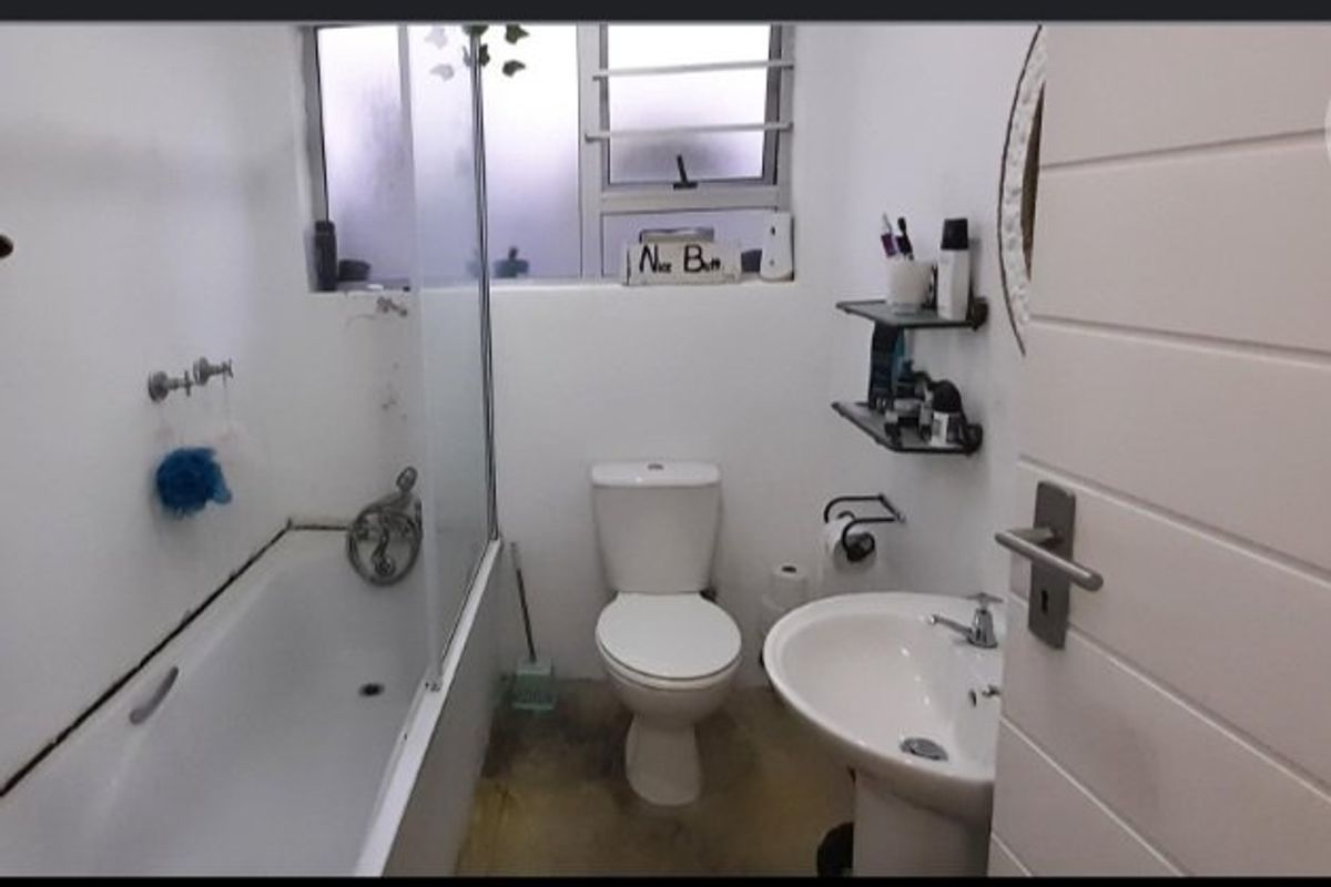 Compact bathroom featuring a bathtub with glass screen, pedestal basin, and toilet. The space requires finishing touches to the flooring and fixtures.