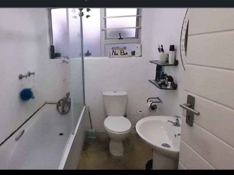 Compact bathroom featuring a bathtub with glass screen, pedestal basin, and toilet. The space requires finishing touches to the flooring and fixtures.