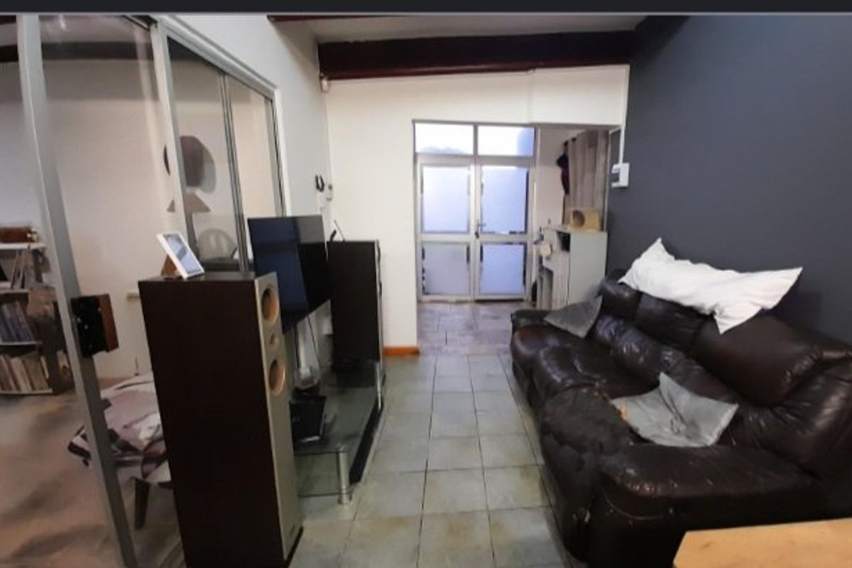 A living area featuring tiled flooring, an exposed ceiling beam, and an aluminium-framed glass door leading to an exterior space.