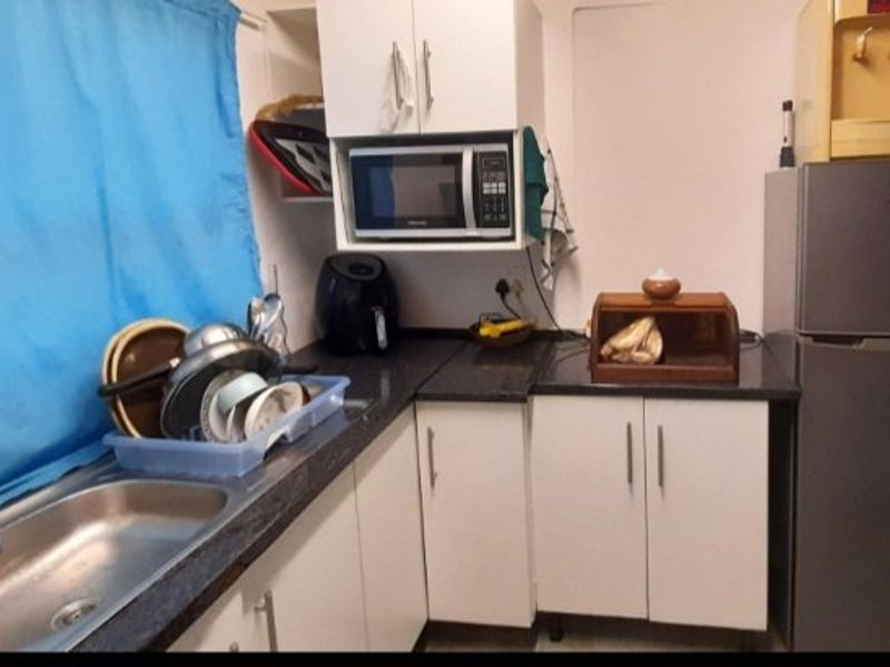 A compact kitchen area featuring white cabinetry, dark laminate countertops, and a stainless steel sink, providing functional preparation and storage space.