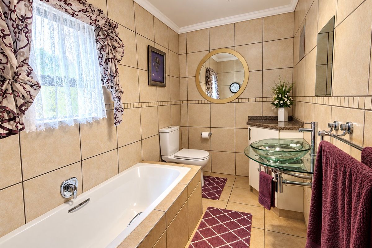 A functional bathroom featuring a built-in bathtub, a glass vessel sink with vanity, and neutral wall-to-wall tiling.