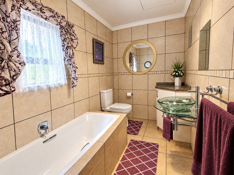 A functional bathroom featuring a built-in bathtub, a glass vessel sink with vanity, and neutral wall-to-wall tiling.