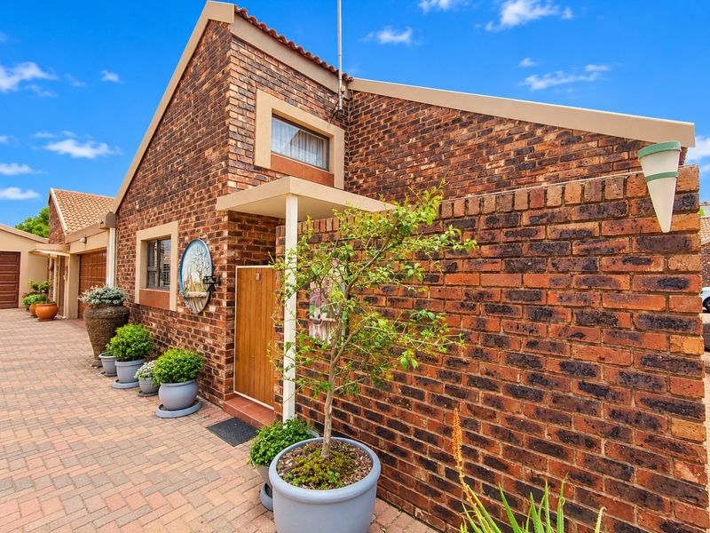 A well-maintained townhouse exterior featuring a classic face brick facade, paved driveway, and a secure wooden entrance door.