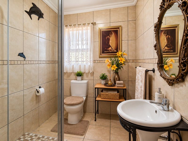A well-maintained bathroom featuring neutral ceramic tiling, a glass-enclosed shower, a pedestal washbasin with chrome fixtures, and a standard toilet.