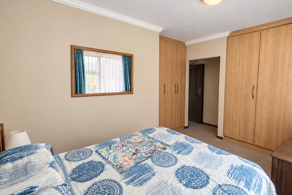 A well-maintained bedroom featuring built-in wooden cupboards, neutral wall tones, and carpeted flooring, offering a functional and comfortable living space.