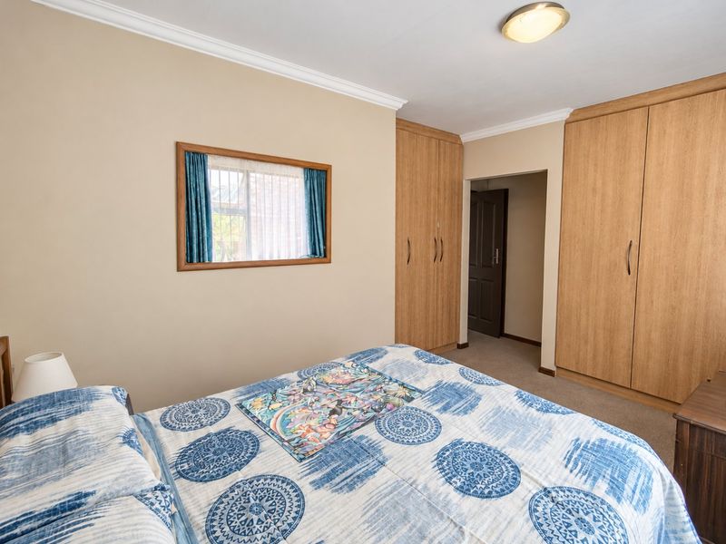 A well-maintained bedroom featuring built-in wooden cupboards, neutral wall tones, and carpeted flooring, offering a functional and comfortable living space.