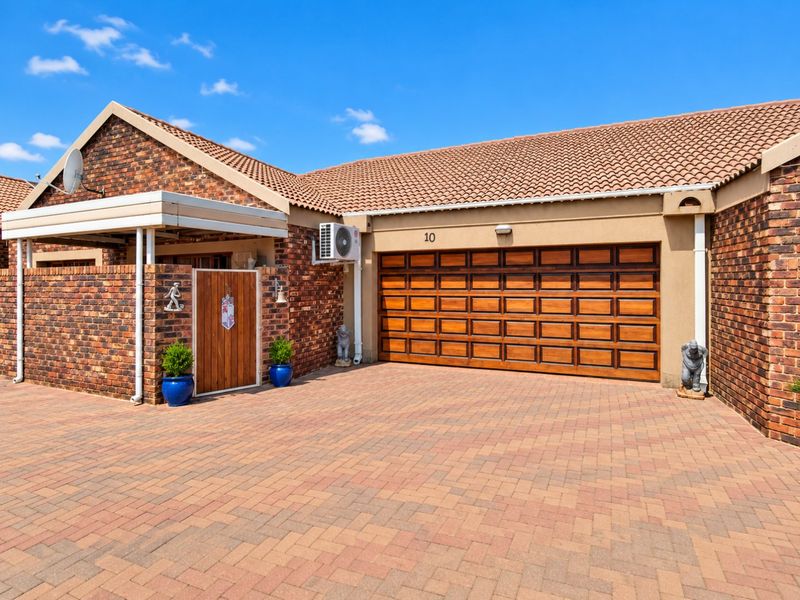 Front exterior view of a townhouse featuring a brick facade, tiled roof, paved driveway, and a wooden sectional garage door.