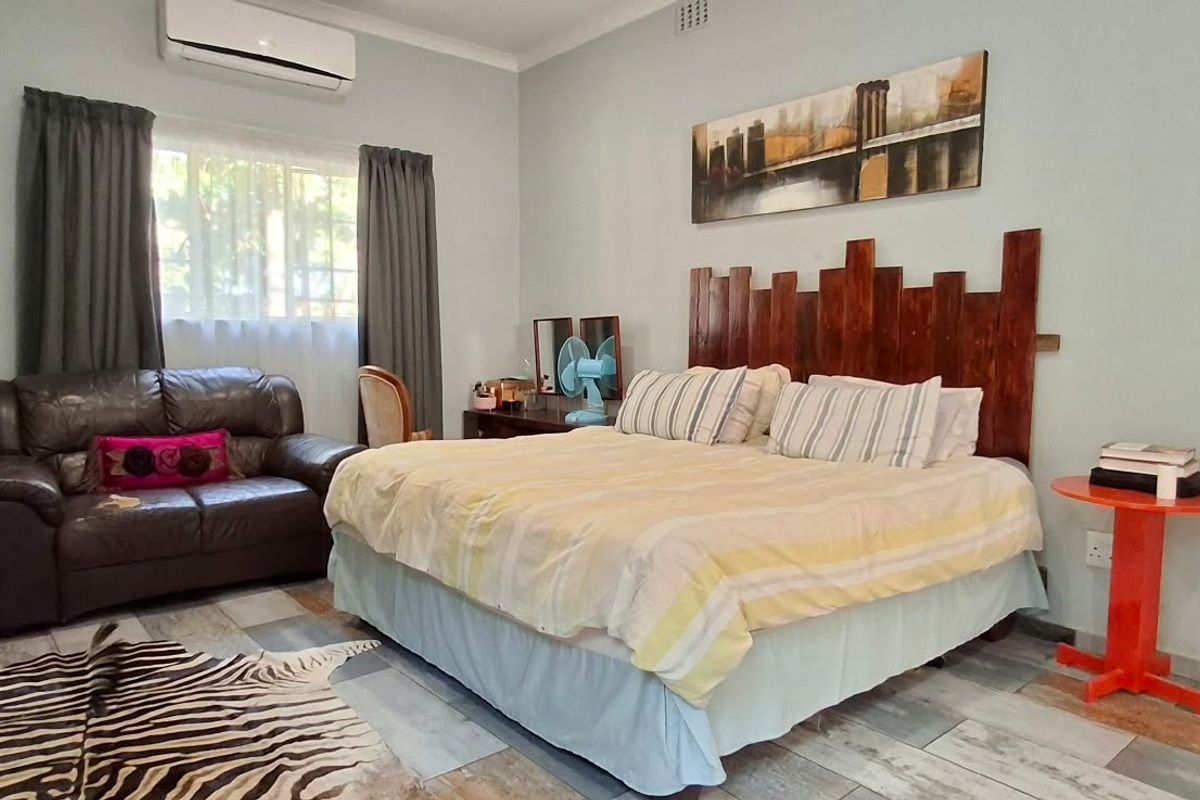 A spacious bedroom featuring tiled flooring, a wall-mounted split-system air conditioner, and large windows with curtain rails.