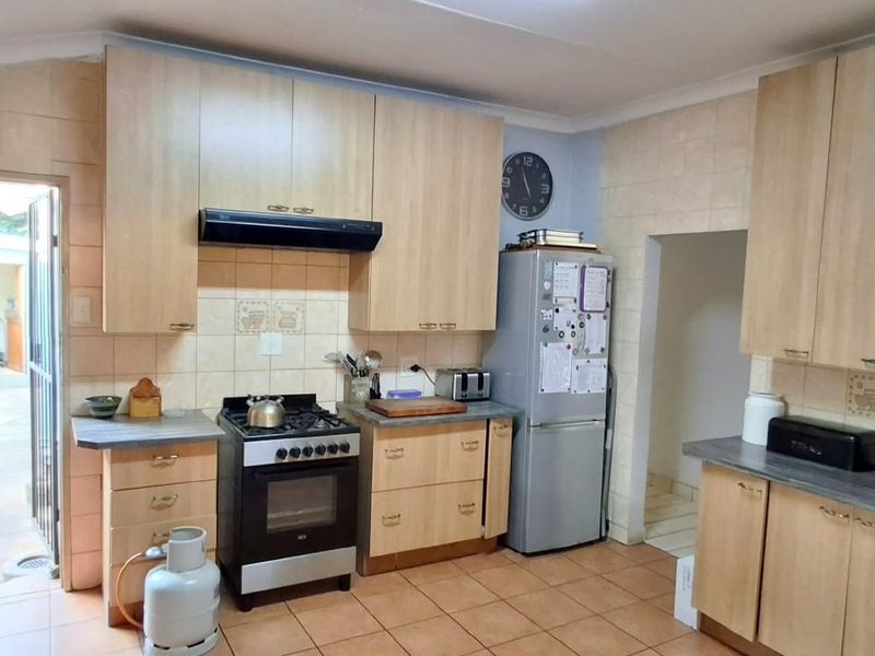 Functional kitchen featuring light wood-finish cabinetry, tiled backsplash, gas stove with extractor fan, and tiled flooring with direct access to the exterior.