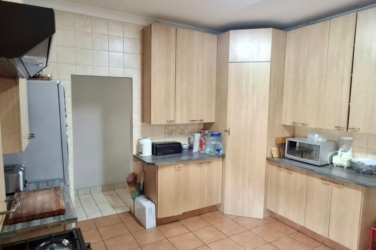 A functional kitchen featuring light wood-look laminate cabinetry, tiled backsplash, and durable floor tiles with a dedicated pantry storage area.
