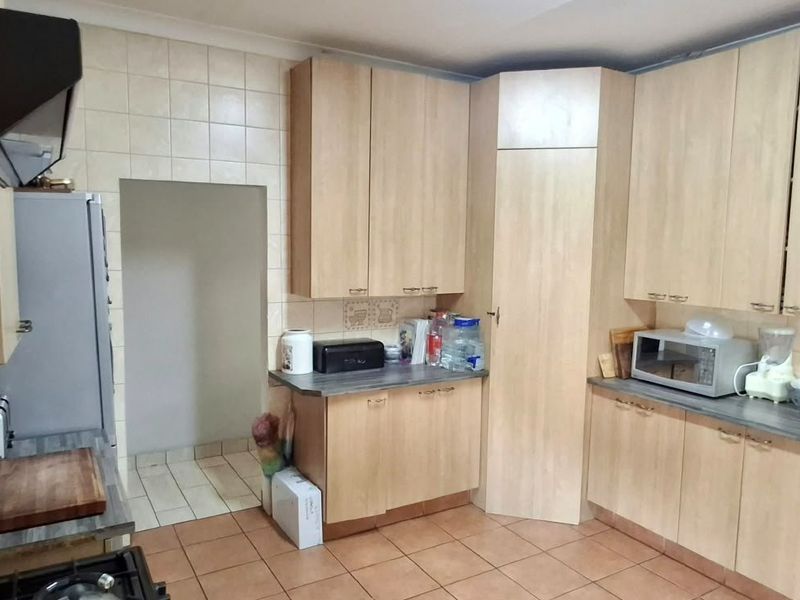 A functional kitchen featuring light wood-look laminate cabinetry, tiled backsplash, and durable floor tiles with a dedicated pantry storage area.