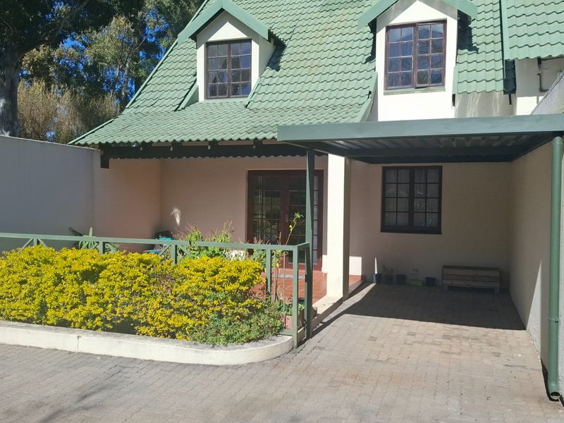 Front view of an apartment featuring a tiled roof, dormer windows, a paved driveway with a carport, and a raised garden bed.
