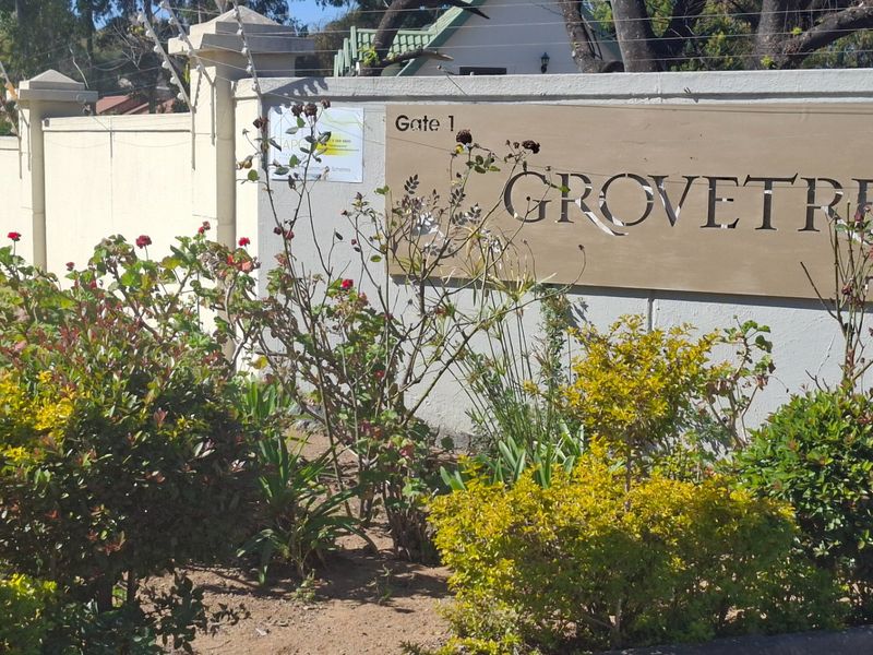 Entrance signage for Grovetree complex featuring a boundary wall with integrated electric fencing and landscaped garden area.