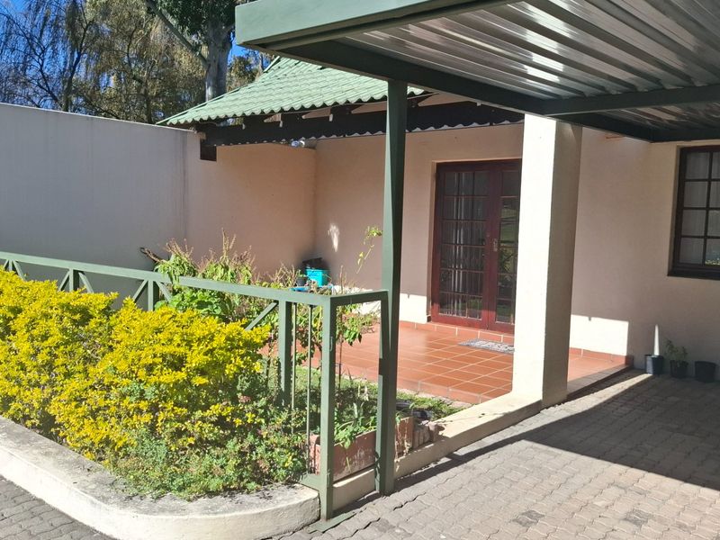 Exterior view of an apartment entrance featuring a covered carport, paved driveway, and a small tiled patio area with metal railings.