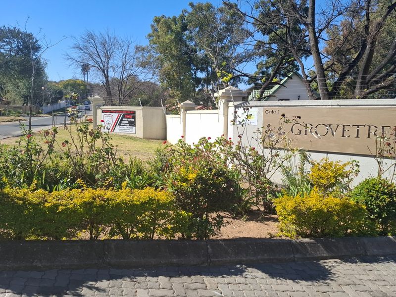 The entrance to Grovetree complex featuring a perimeter wall, electric fencing, and clear signage from the street.
