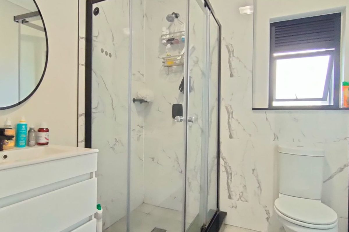 Modern bathroom featuring a glass shower enclosure, vanity cabinet with basin, toilet, and marble-look wall tiling.