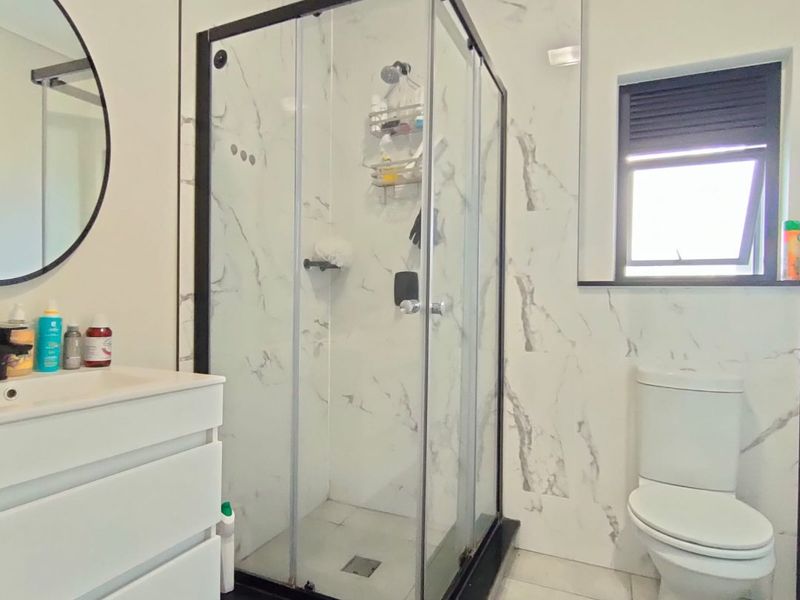 Modern bathroom featuring a glass shower enclosure, vanity cabinet with basin, toilet, and marble-look wall tiling.