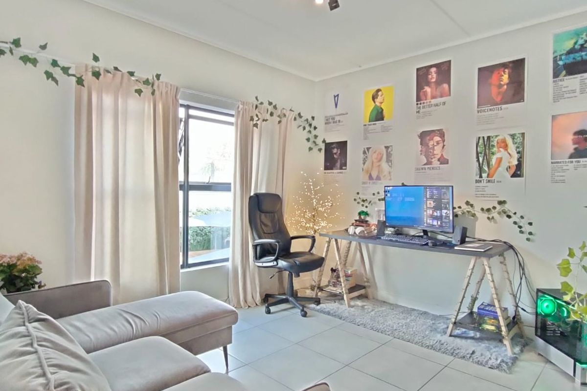 A bright living room featuring neutral tiled flooring, modern track lighting, and a large window, creating a comfortable and functional living space.