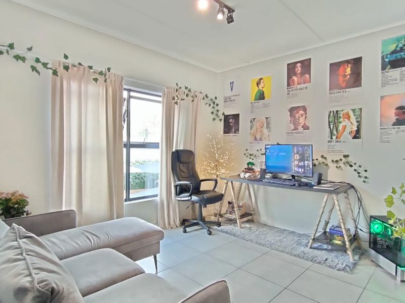 A bright living room featuring neutral tiled flooring, modern track lighting, and a large window, creating a comfortable and functional living space.