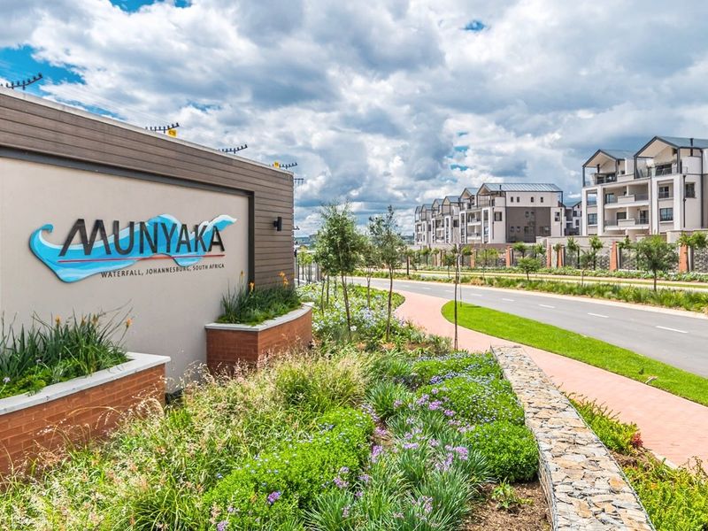 Entrance view of Munyaka estate in Waterfall, Johannesburg, featuring modern signage, manicured landscaping, and paved walkways leading to residential apartment blocks.