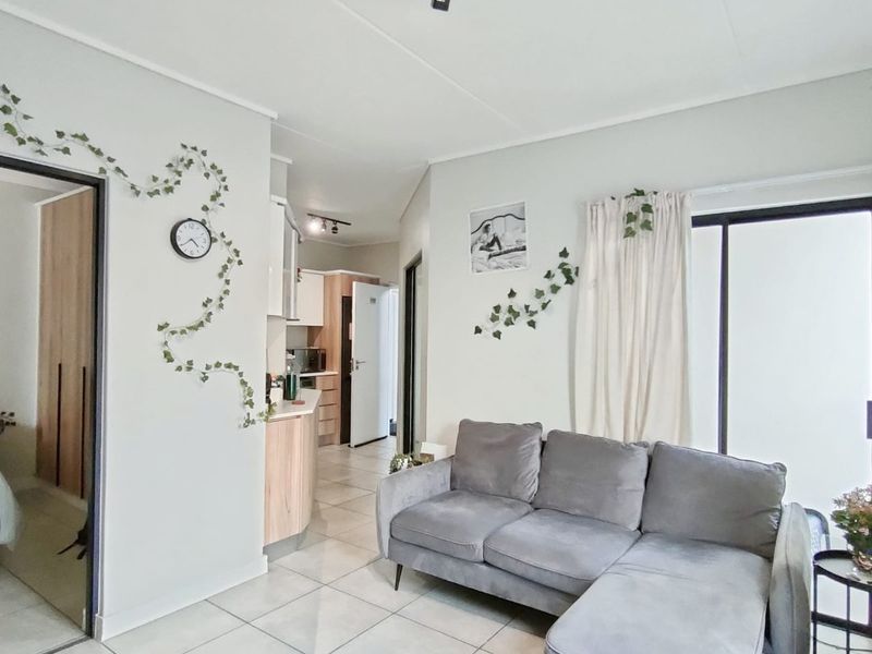 An open-plan living area featuring tiled flooring, track lighting, and a sliding glass door, with a view into the adjacent kitchen space.