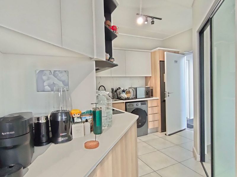 Modern kitchen featuring light wood-tone cabinetry, stone-look countertops, tiled flooring, and an integrated washing machine, offering a clean and functional workspace.