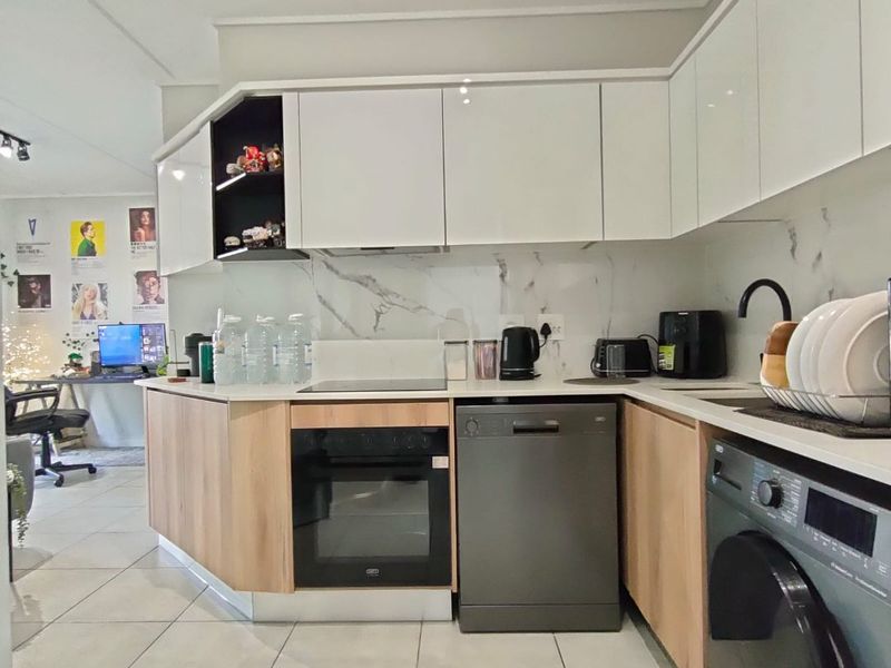 Modern kitchen featuring white gloss cabinetry, wood-tone lower units, marble-look splashback, and integrated appliances with tiled flooring.