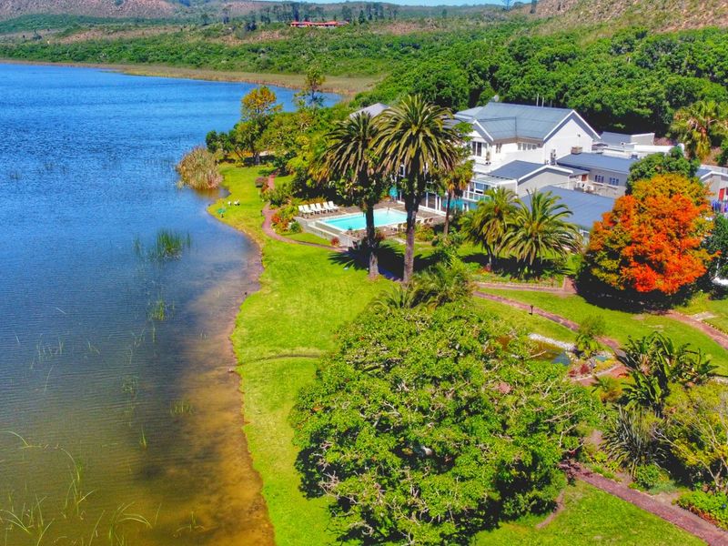 Aerial view of a sprawling lakefront property featuring a swimming pool, extensive landscaped gardens, and mature trees along the water's edge.