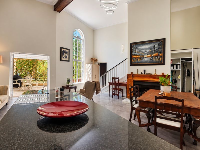 Spacious open-plan living and dining area featuring high ceilings, an arched window, a fireplace with a timber mantel, and direct access to a patio.