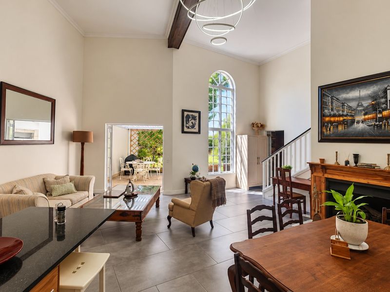 Spacious open-plan living and dining area featuring high ceilings, an arched window, a fireplace with a wooden mantel, and direct access to a patio.