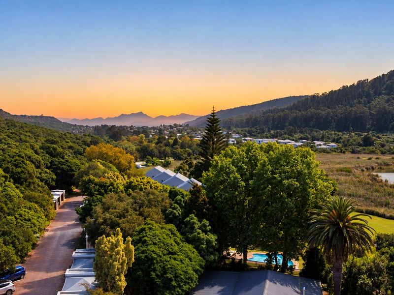 An elevated aerial view showcasing the property's surrounding landscape, including a swimming pool, driveway, and lush natural greenery at sunset.
