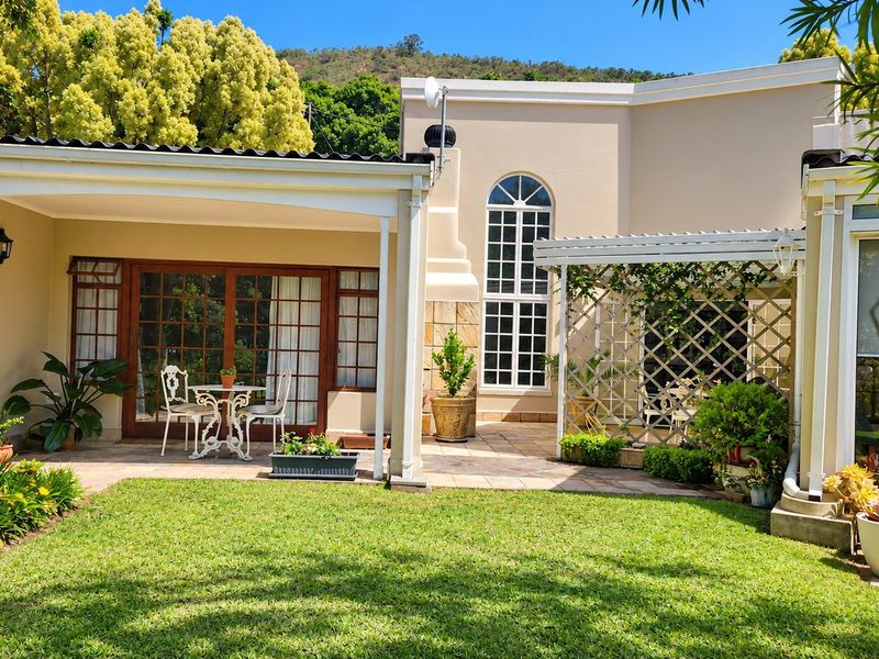 A well-maintained rear exterior featuring a covered patio, a decorative pergola with lattice, and a landscaped garden area with paved flooring.